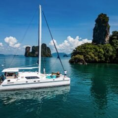 Nyami Charter catamaran phuket slow cruise against a backdrop of chicken island aon nang, krabi with other limestone islands in the distance on a beautiful day with fluffly clouds and bright blue sky