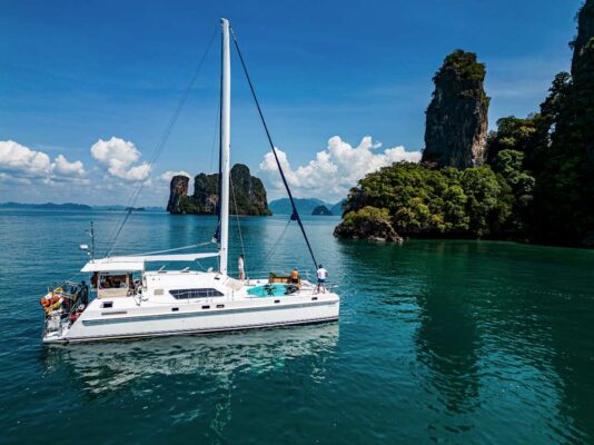 Nyami Charter catamaran phuket slow cruise against a backdrop of chicken island aon nang, krabi with other limestone islands in the distance on a beautiful day with fluffly clouds and bright blue sky