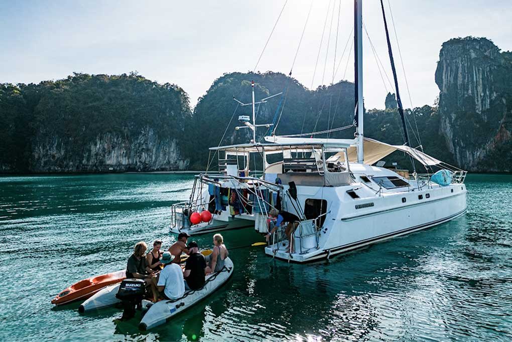 Nyami's 15hp rib plus a kayak returning to Nyami's stern and swim decks with the catamaran anchored in a secluded bay surrounded by limestone cliffs