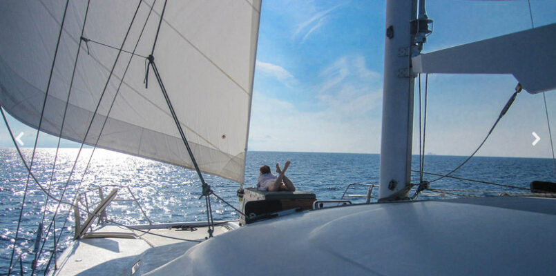 nyami 55ft charter catamaran heading home at early sunset with blue skies and calm water viewed across the foredeck with guest relaxing on bow