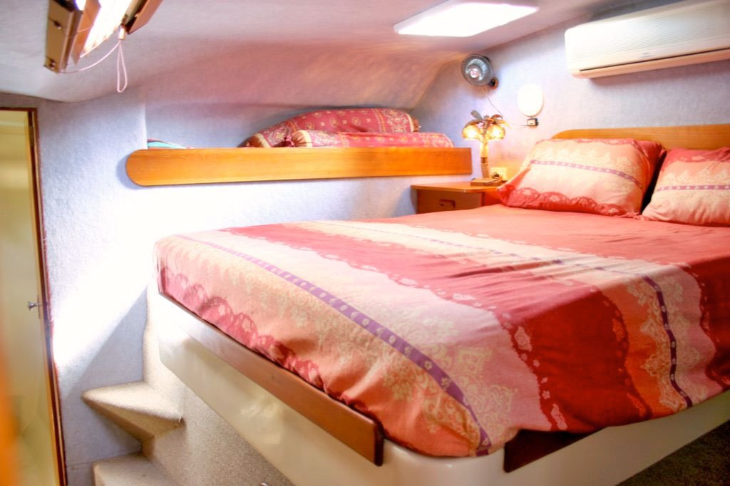 view of raised king size bed in luxury cabin with fan, storage space and attractive bed linen in reds, oranges, pink and purple