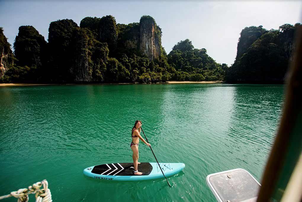 feamle guest launching from stern of 55ft charter catamaran nyami which is anchored off a secluded, sandy beach in Phang Nga Bay near Thailand
